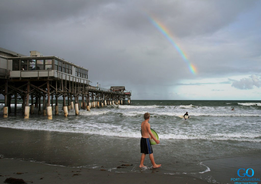 Surfers in the Atlantic Ocean under a rainbow near the Cocoa Beach Pier