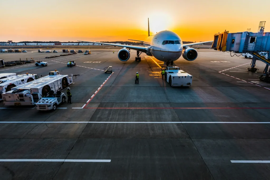 front of airplane jetway and support vehicles on tarmac with sun rising behind