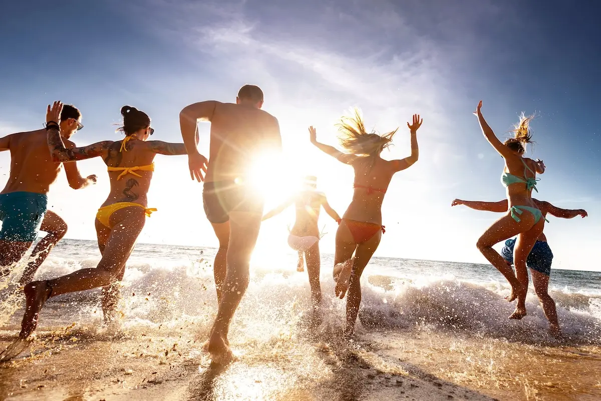 group of friends on beach running into the ocean