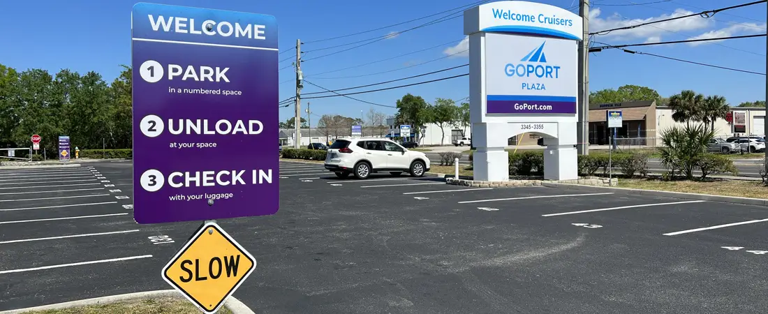 Parking spaces in Port Canaveral parking lot with large sign that says Go Port Plaza and smaller sign that says Welcome with instructions to Park Unload Check In