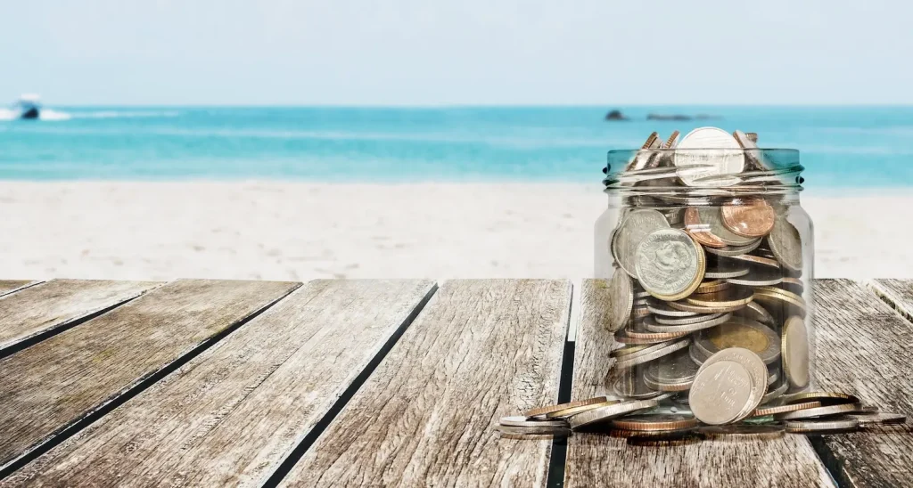 Jar of coins sitting on wooden table on beach with ocean in the background