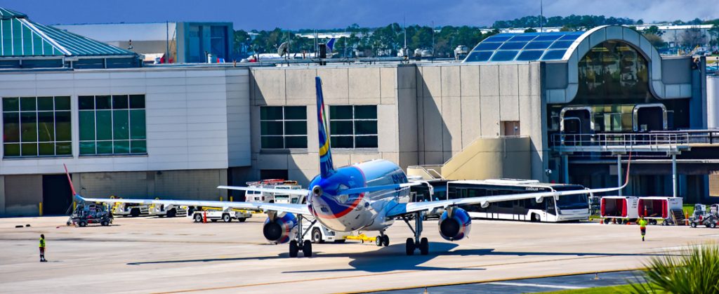 Blue airplane taxiing to the gate at Orlando airport with airport terminal building in the background