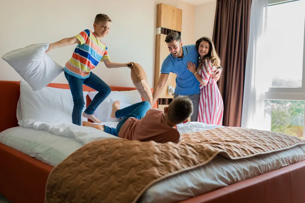 Two kids having pillow fight on the hotel room bed while parents watch